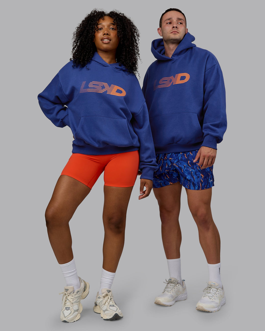 Duo wearing Unisex Motion Hoodie Oversize - Galactic Cobalt-Vibrant Orange