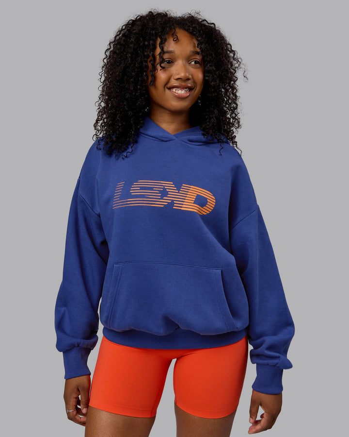 Woman wearing Unisex Motion Hoodie Oversize - Galactic Cobalt-Vibrant Orange
