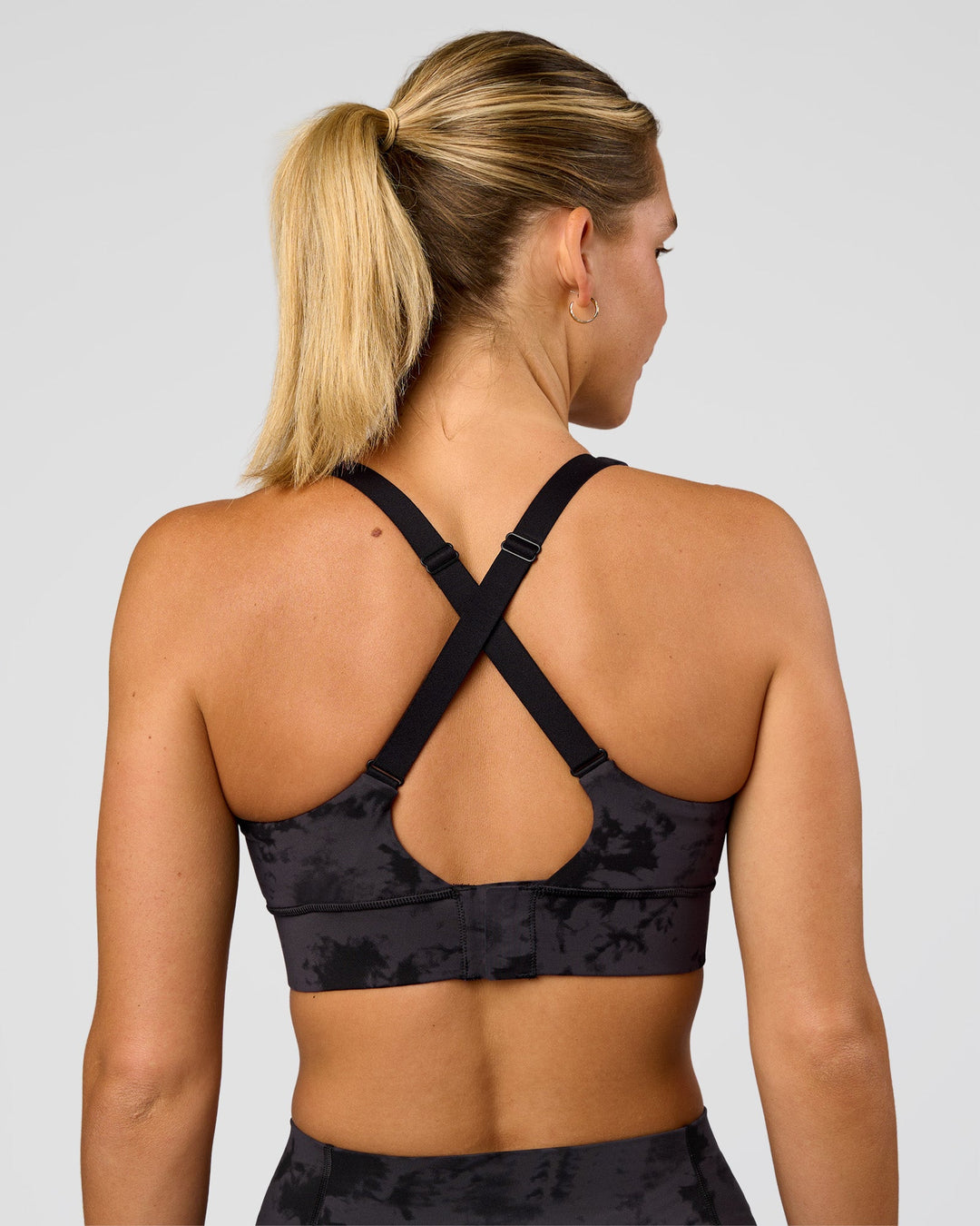 Woman wearing Accelerate Sports Bra - Black Tie Dye | Set:true | Angle:back | Model:Amity | Size:S