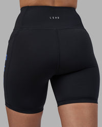 Woman wearing Rep Ultra High-Rise 6" Short Pockets - Black-Power Cobalt | Model:Rhiley | Size:S